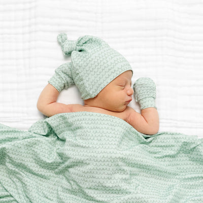 Newborn baby wrapped in a green textured blanket and wearing a matching hat on a white background