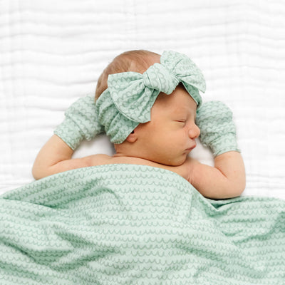 Newborn baby wrapped in a green textured blanket with a matching headband on a white background