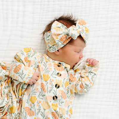 Newborn baby wrapped in a floral swaddle with a matching headband on a white background