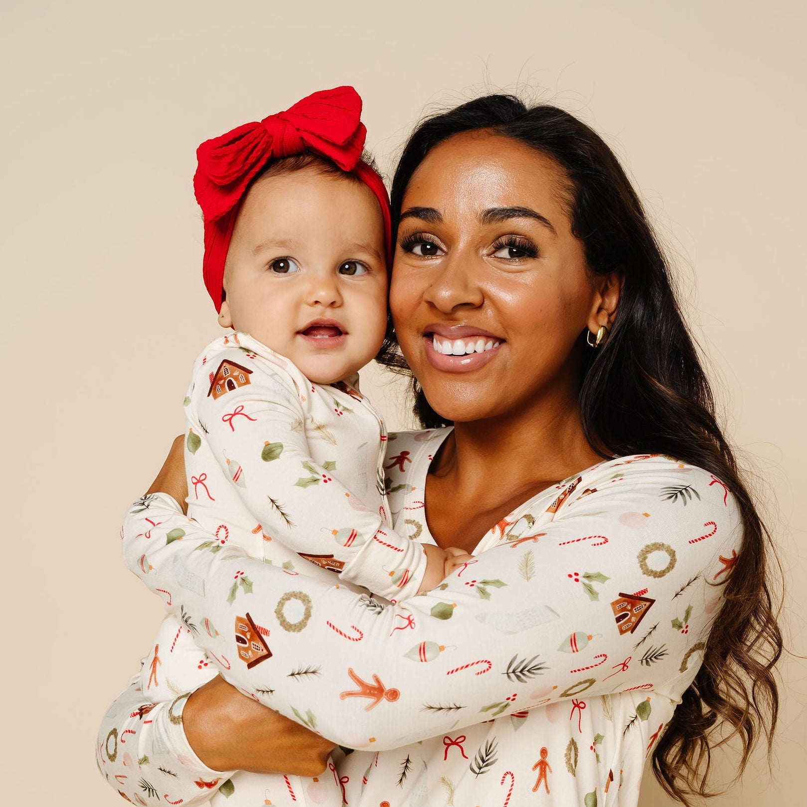 Woman and child wearing matching pajamas with a festive pattern against a beige wall.