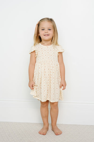 Young girl wearing a yellow dress with ruffled sleeves against a white background