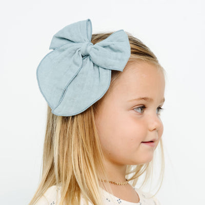 Young girl wearing a large light blue bow headband against a white background