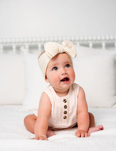 Baby wearing a white outfit with buttons and a bow headband on a white background