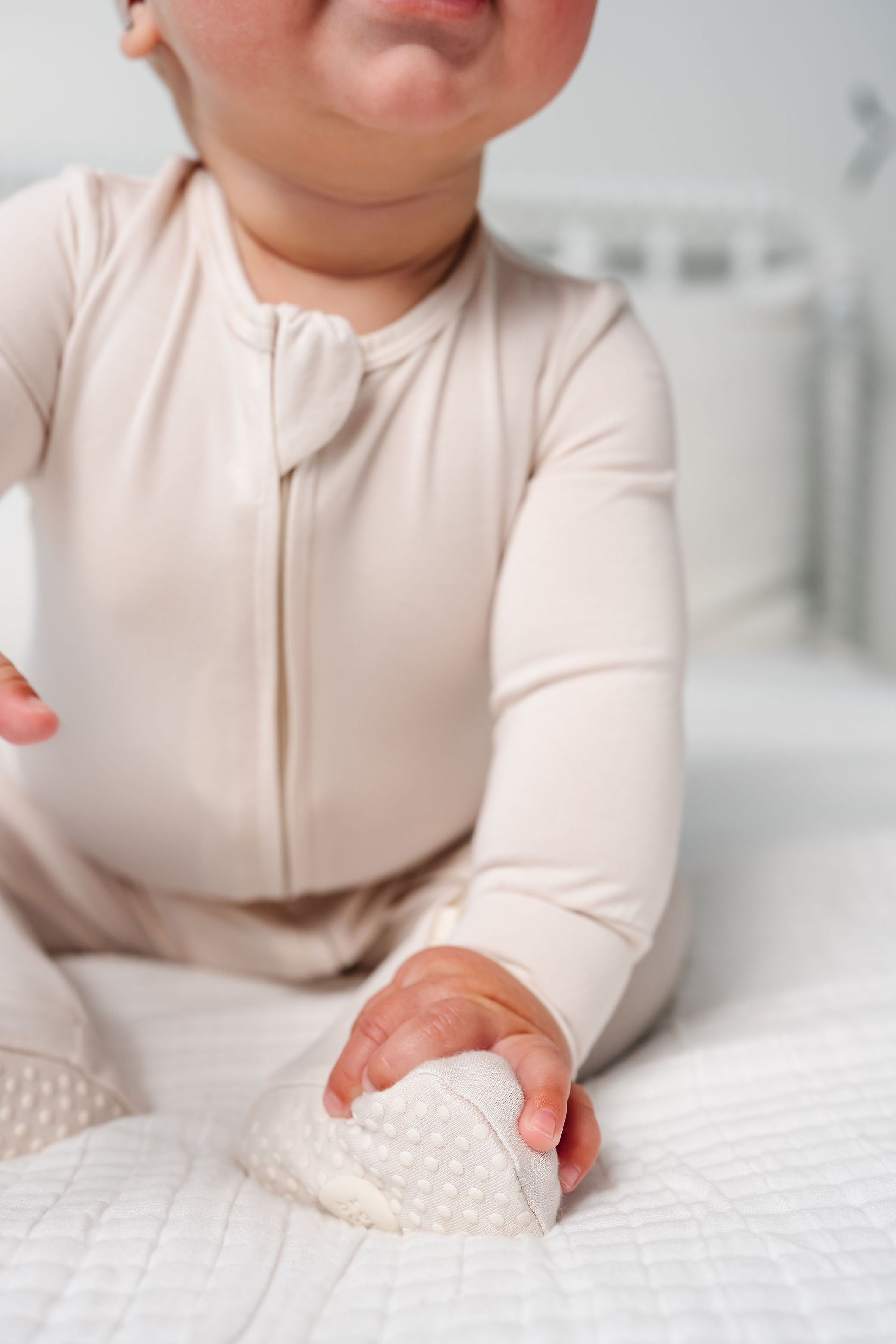 Baby in a white outfit holding a textured white object on a white blanket.