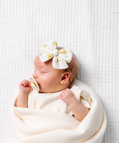 Newborn baby wrapped in a white blanket with a decorative headband on a white background
