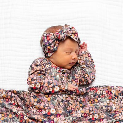 Newborn baby wrapped in a floral blanket with a matching headband on a white background