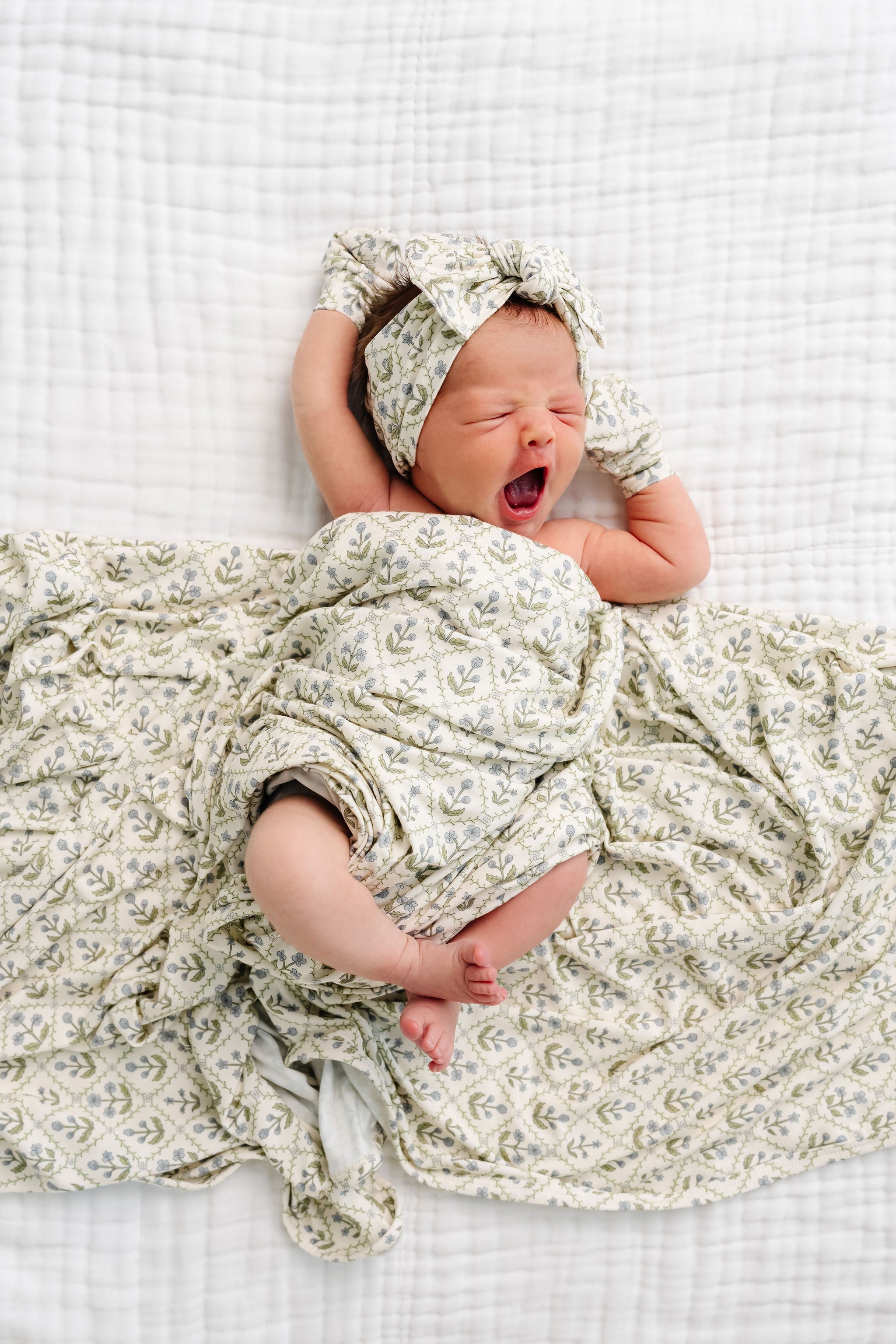 Newborn baby wrapped in a floral blanket and headband on a white checkered background