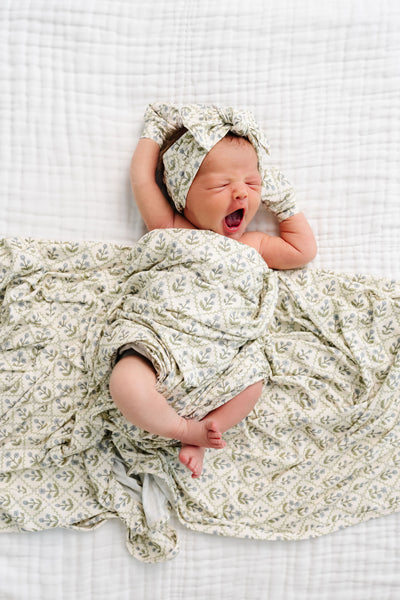 Newborn baby wrapped in a floral blanket and headband on a white checkered background