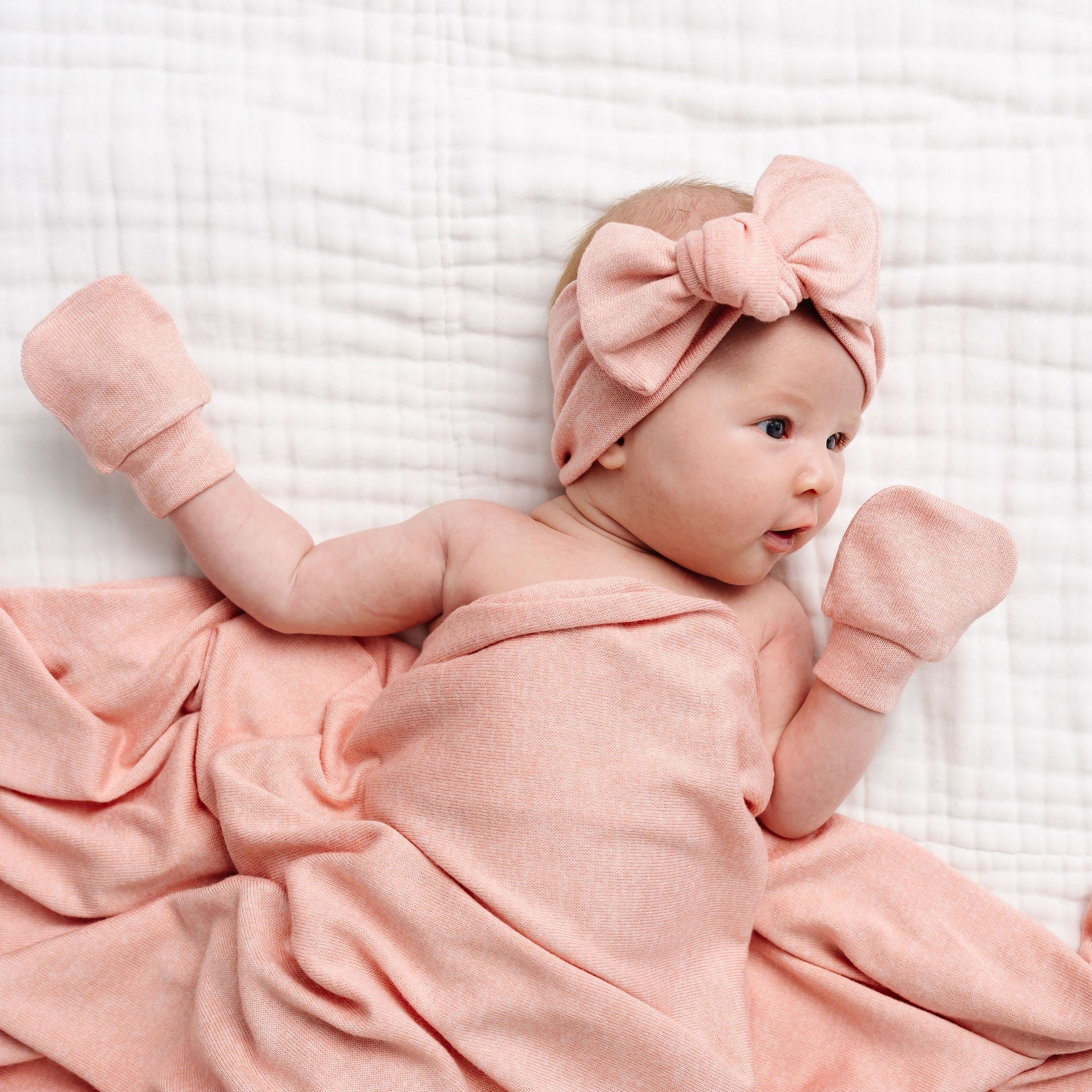 Baby wrapped in a pink blanket with a matching headband on a white textured background