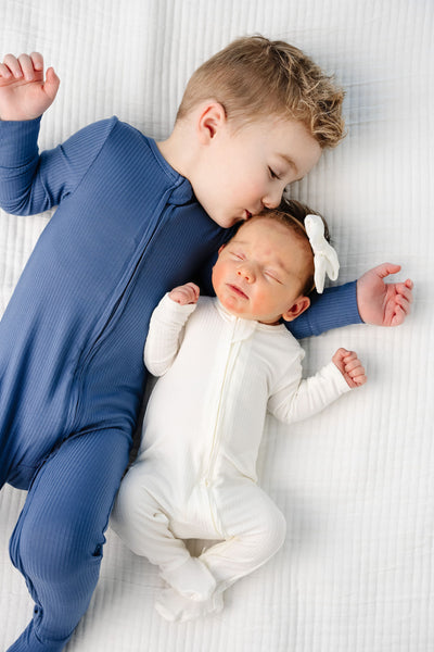 Harrison Zipper Footies Toddler boy in 2T size kissing little newborn in wren newborn size