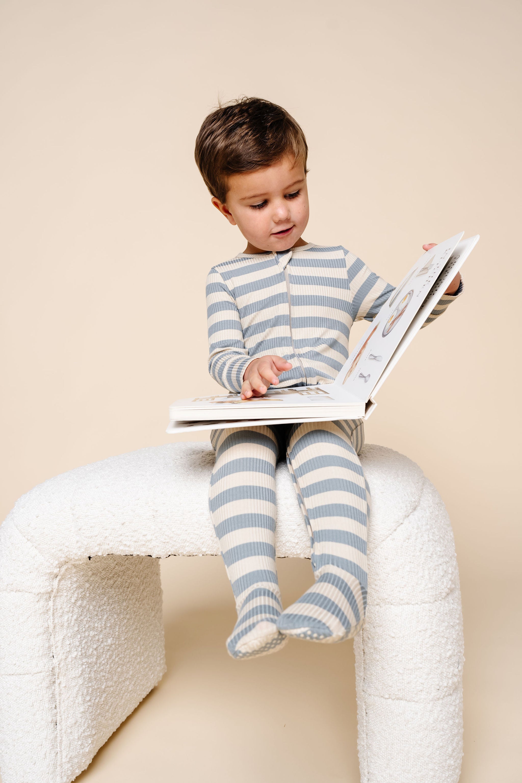 lincoln zipper footies toddler boy sitting on stool reading a book.