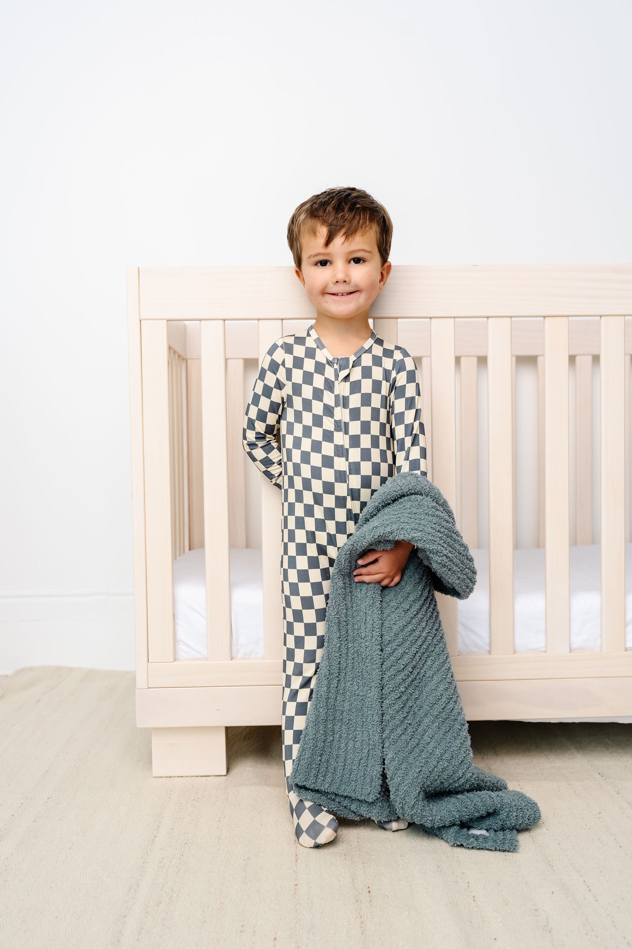 miles zipper footies toddler boy standing next to crib with ocean chenille