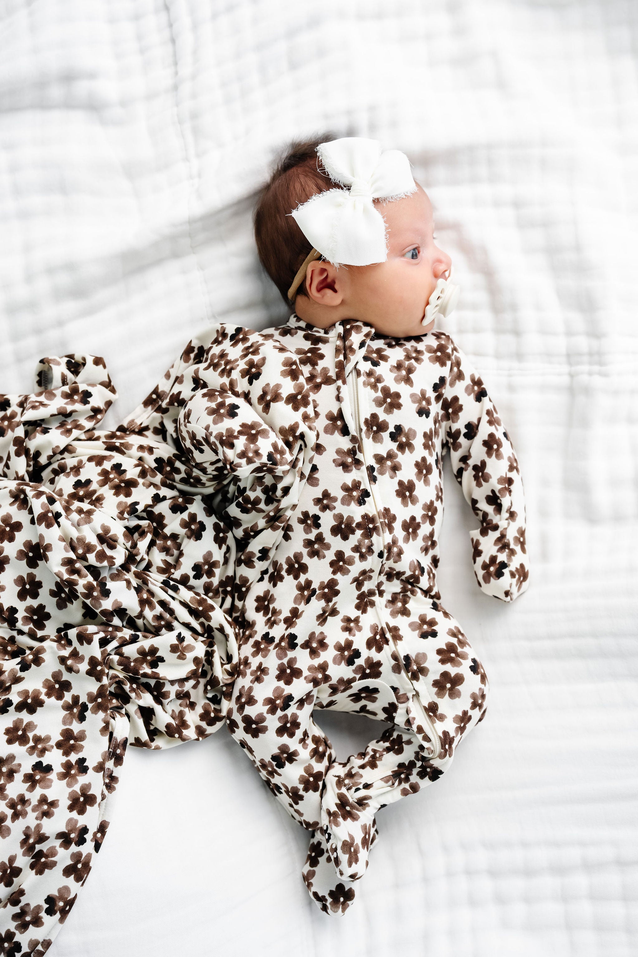 sloane zipper footies newborn girl with chiffon bow laying on bed with matching sloane swaddles