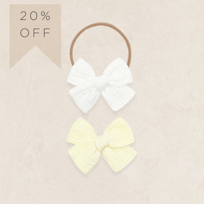 Two hair bows, one white and one yellow, on a beige background with a 20% off label.