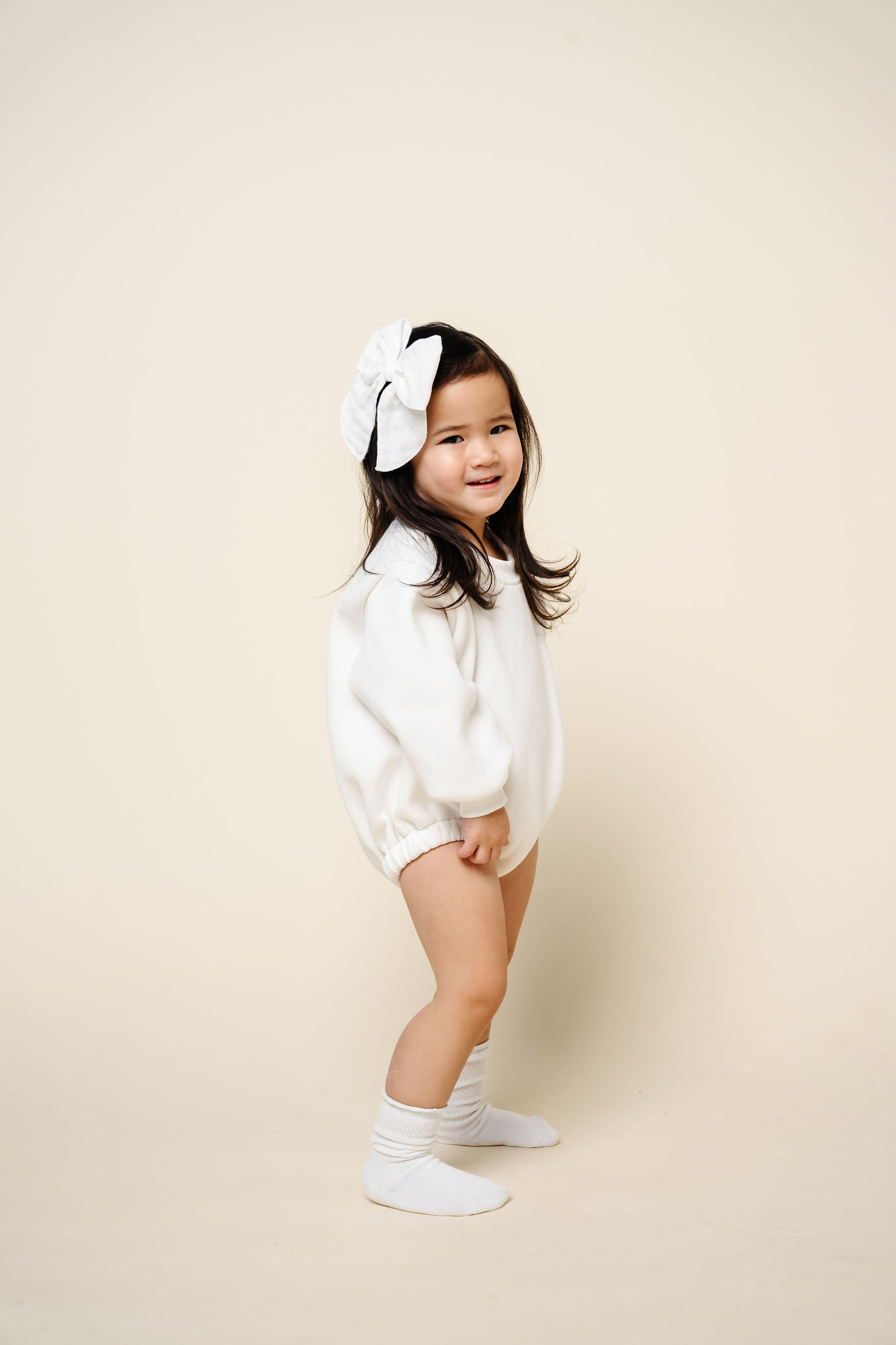 white sweatshirt romper toddler girl standing dark hair