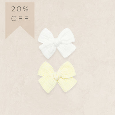 Two hair bows, one white and one yellow, on a beige background with a 20% off label.