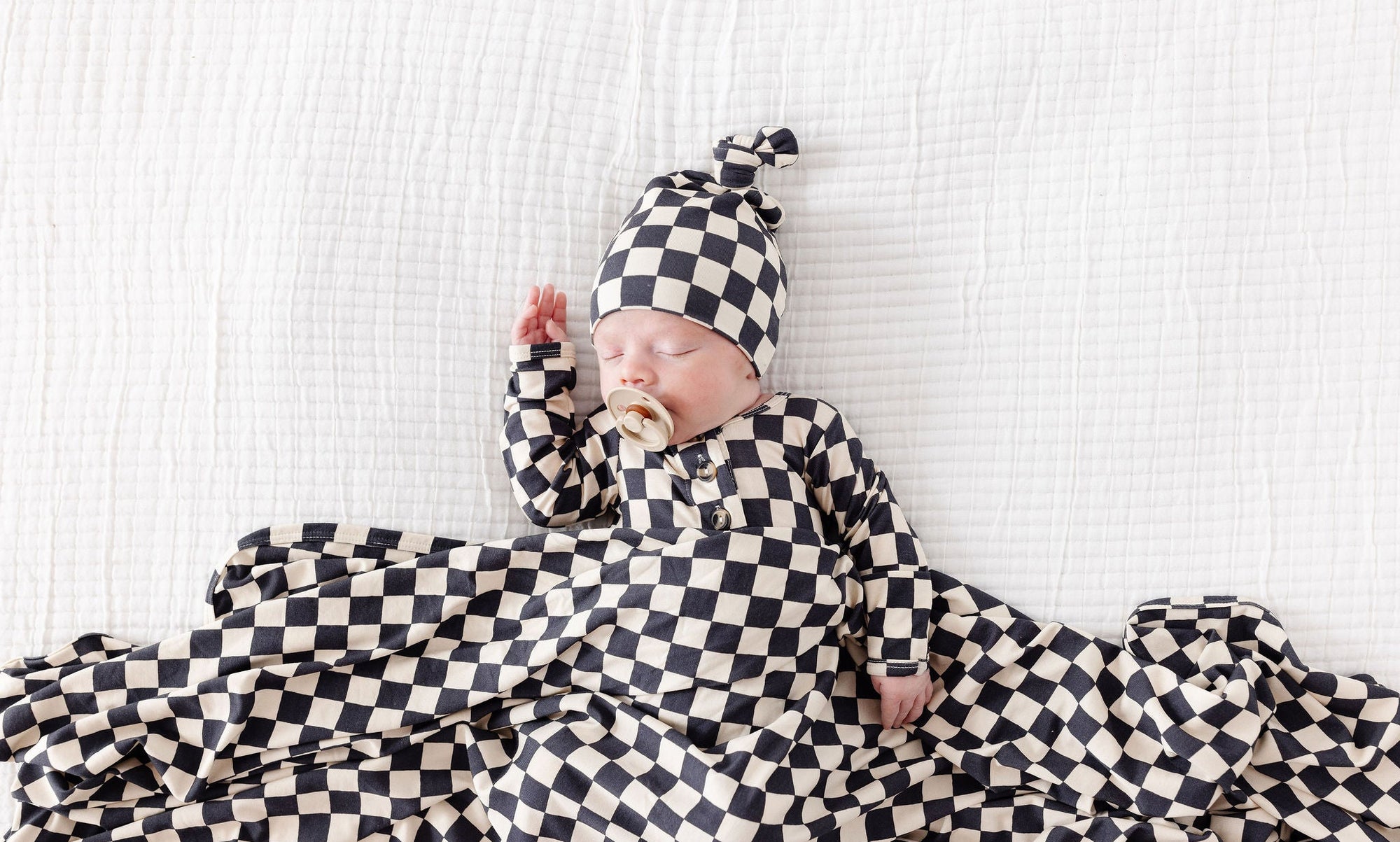 Newborn baby wrapped in a black and white checkered blanket and hat on a light background