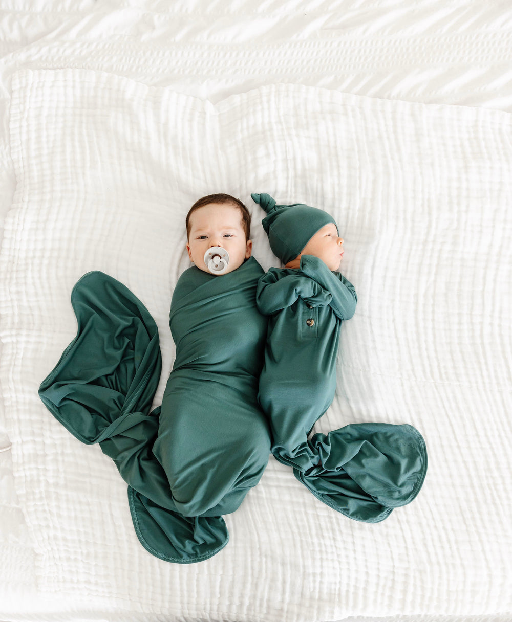 Two babies wrapped in green swaddles on a white textured surface