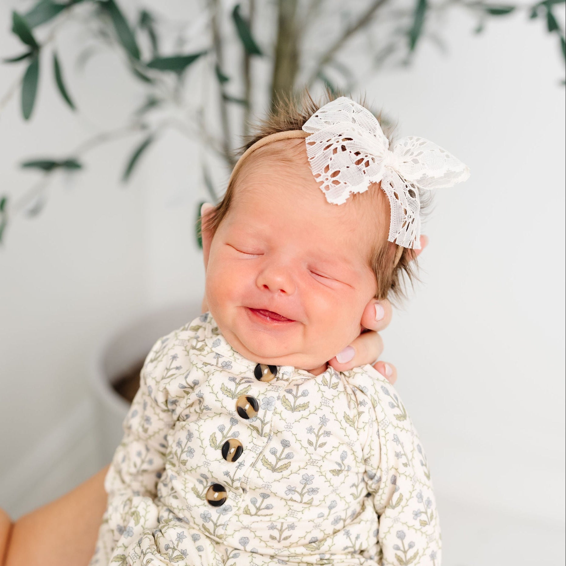 Newborn baby wrapped in a white lace blanket with a headband, lying on a soft surface.