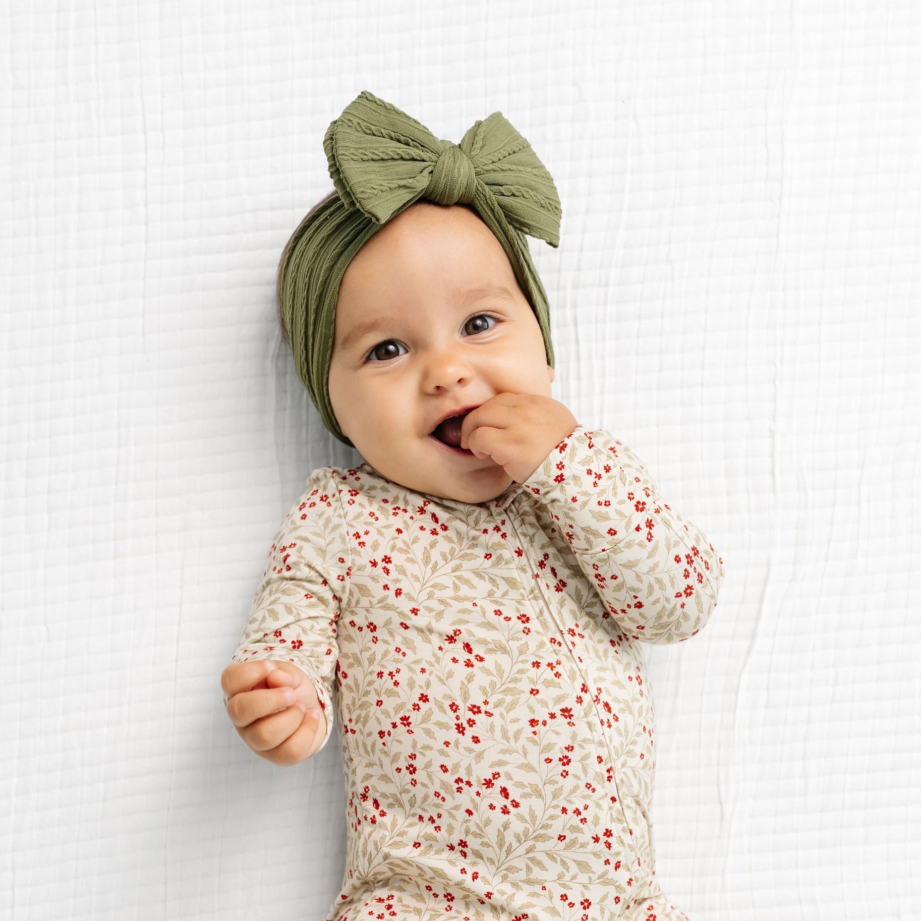 Baby wearing a floral onesie and green headband on a white background