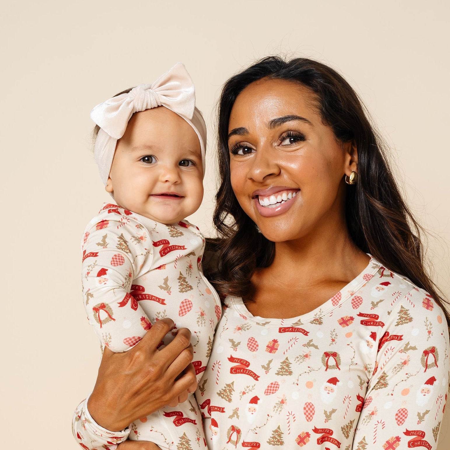 Woman holding a baby both wearing matching pajamas against a beige background
