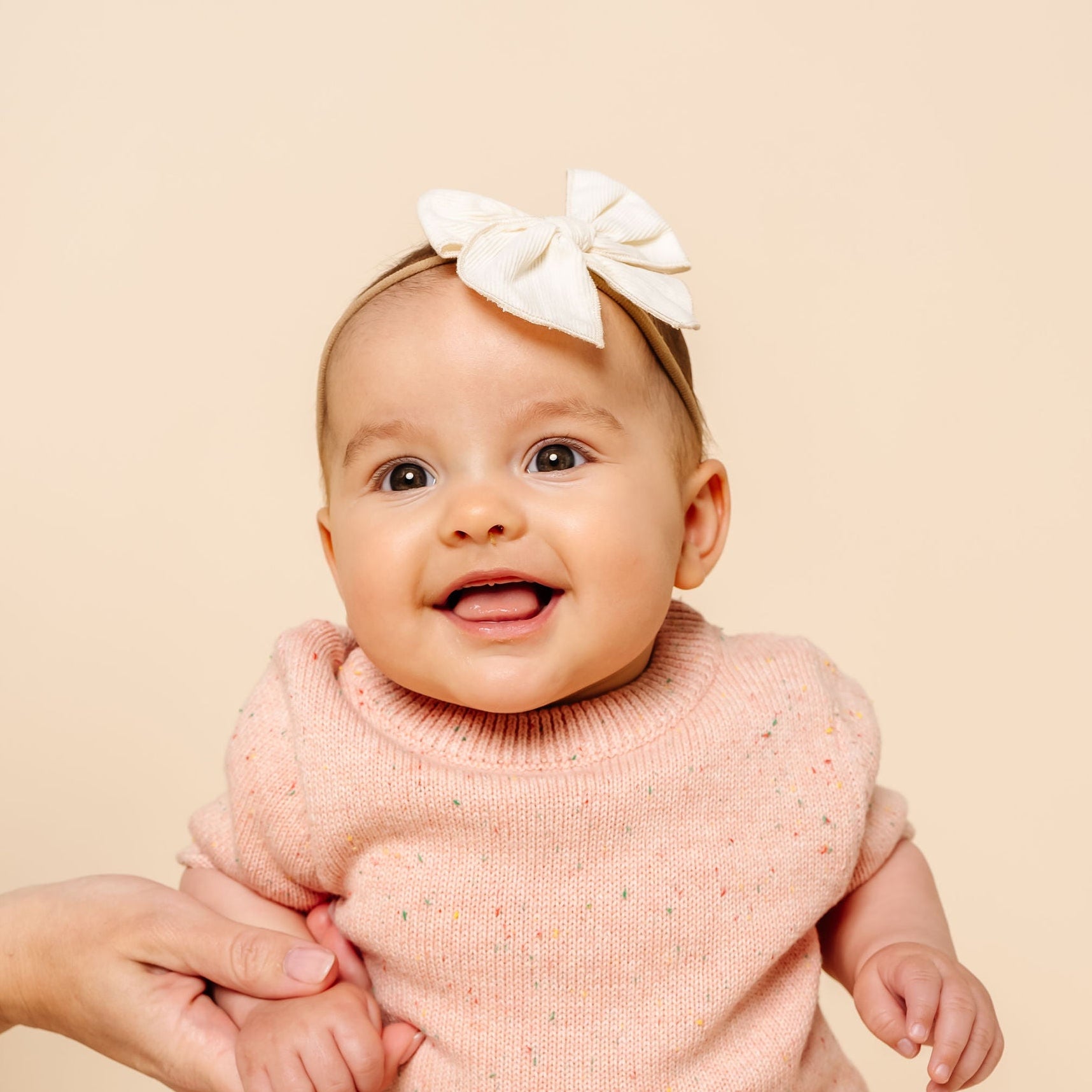 Baby in a pink outfit with a white bow sitting on a beige surface
