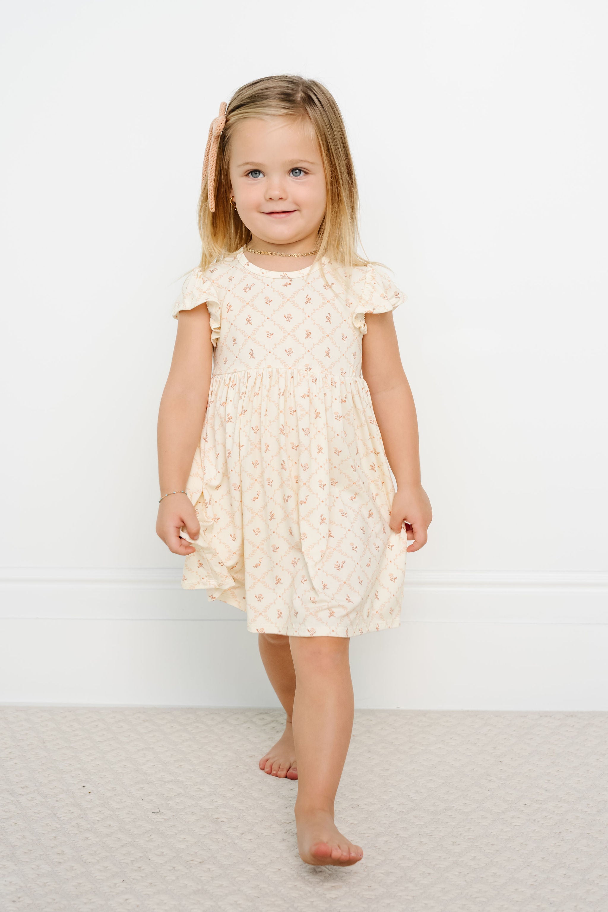 Young girl wearing a cream-colored dress with ruffled sleeves against a white background
