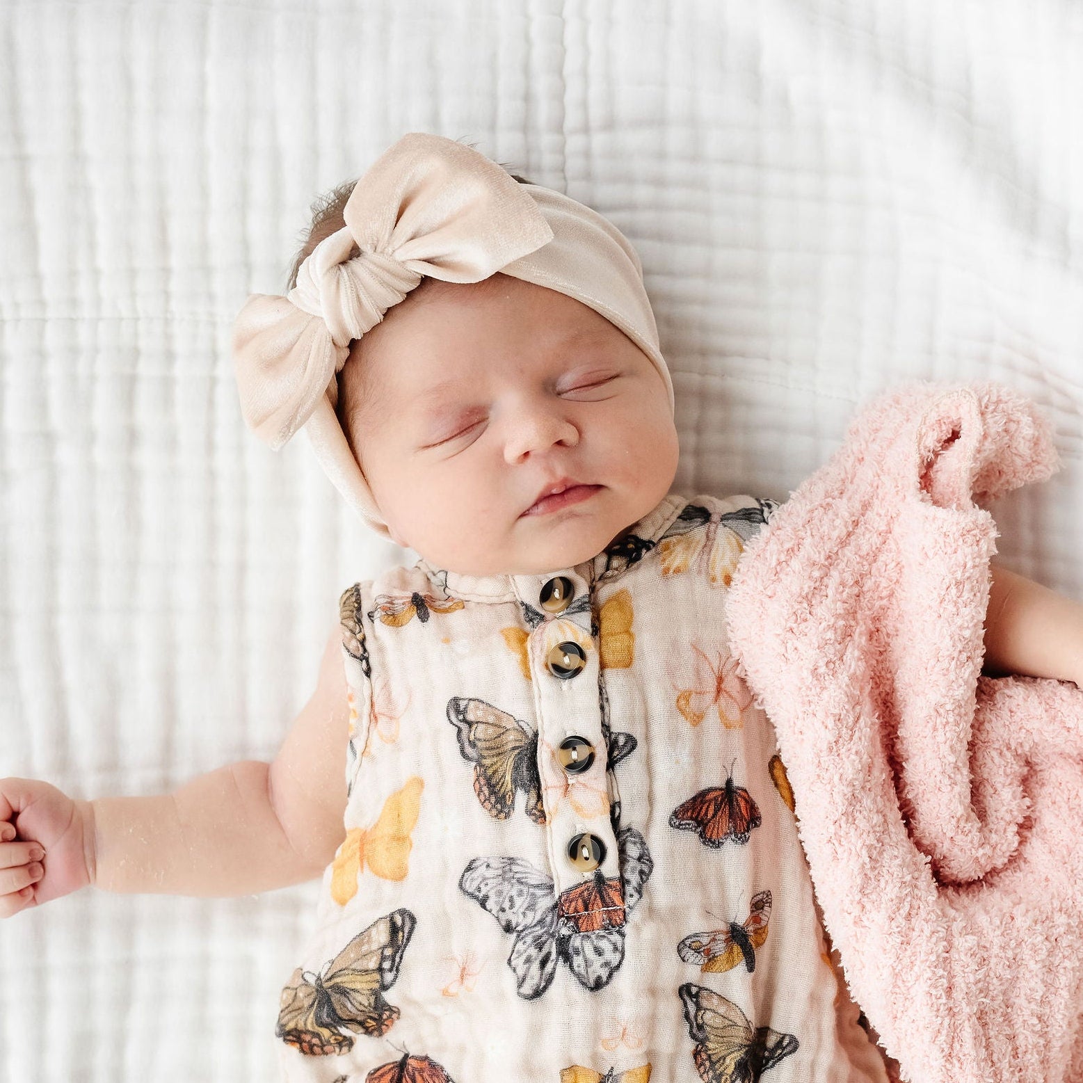 Newborn baby wearing a butterfly-patterned onesie on a white blanket