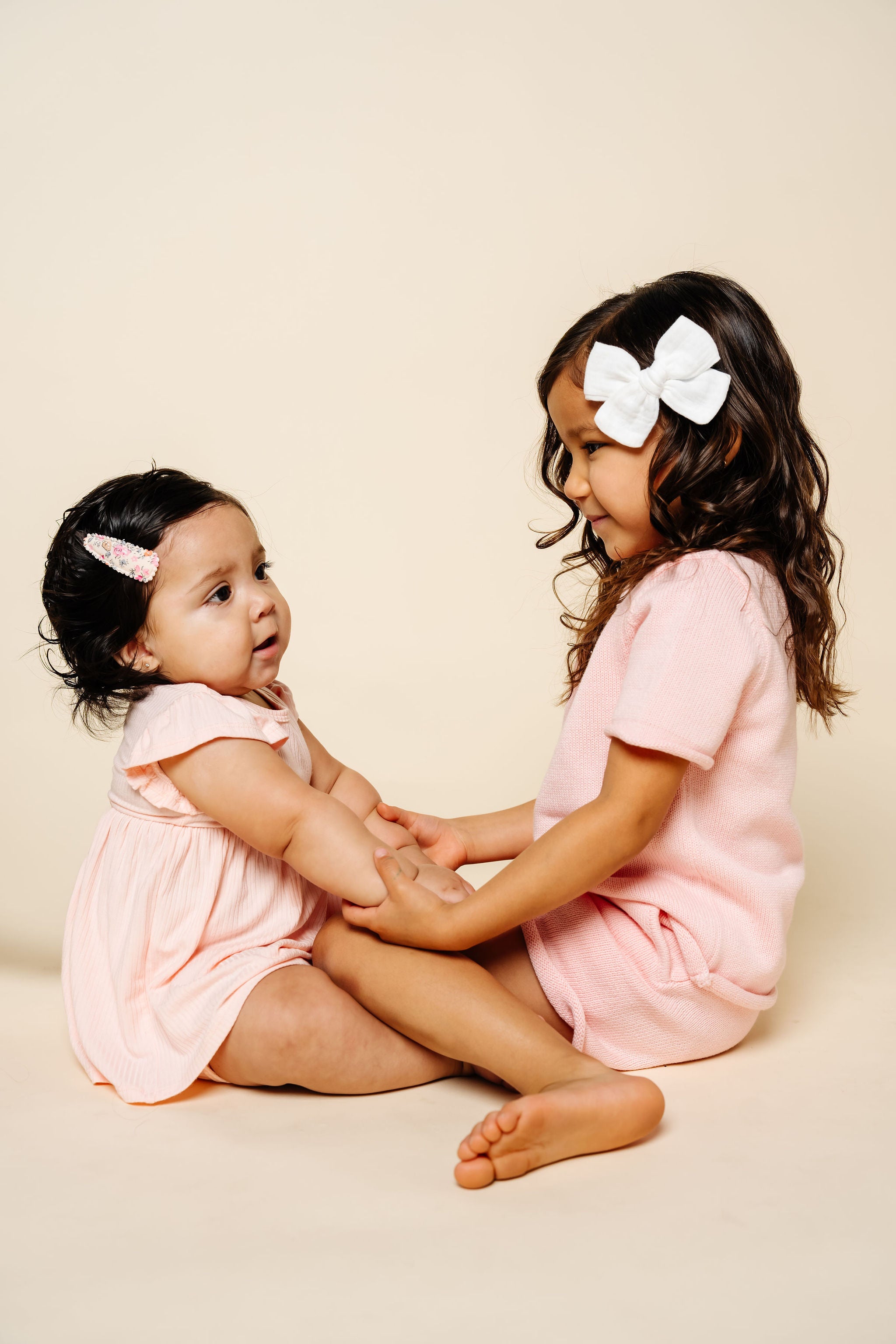 Two young girls in matching pink outfits sitting on a beige background
