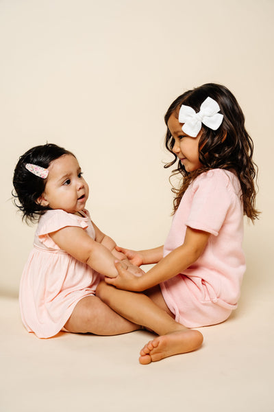 Two young girls in matching pink outfits sitting on a beige background