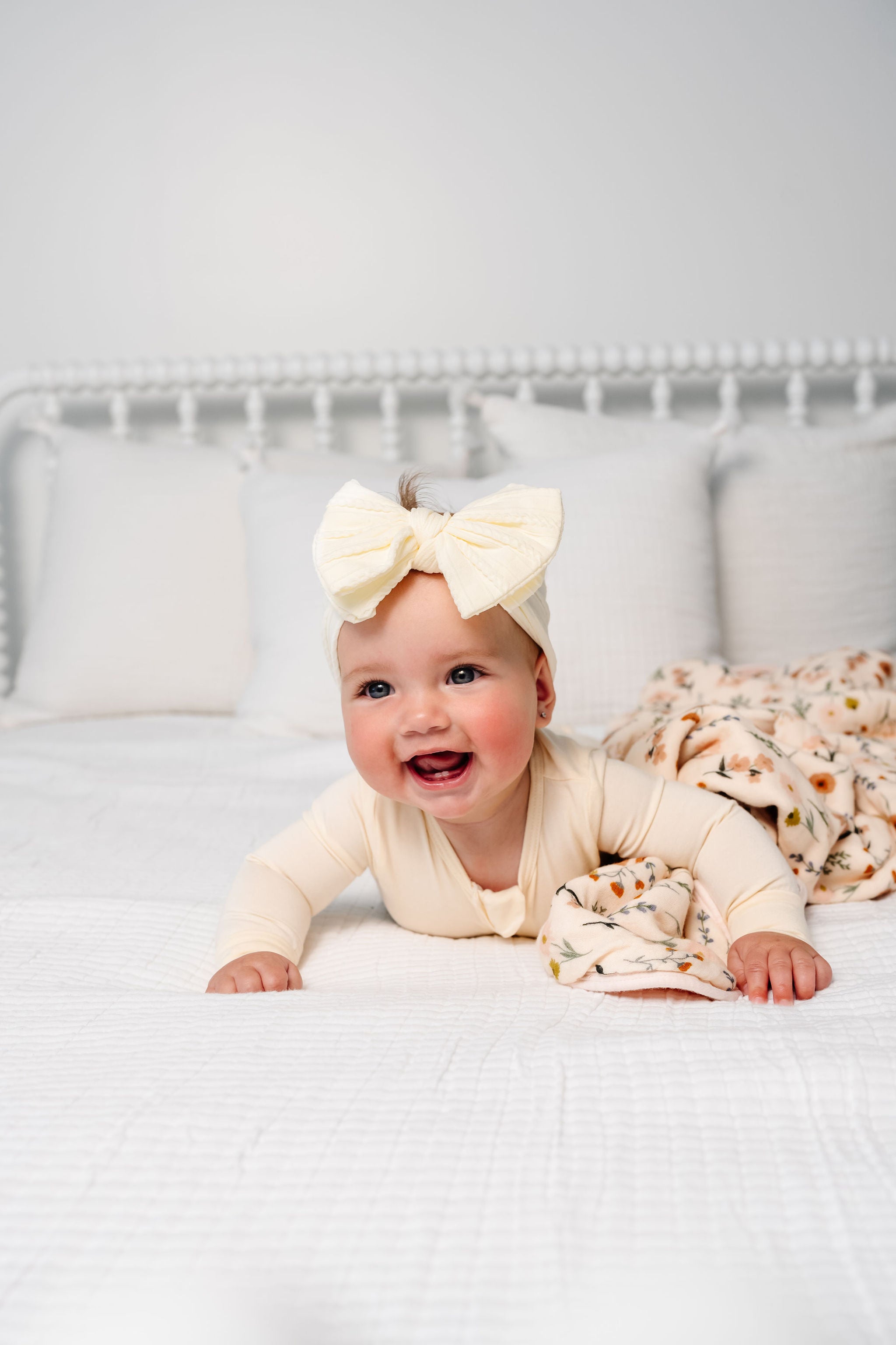 Baby wearing a large bow headband on a white bed