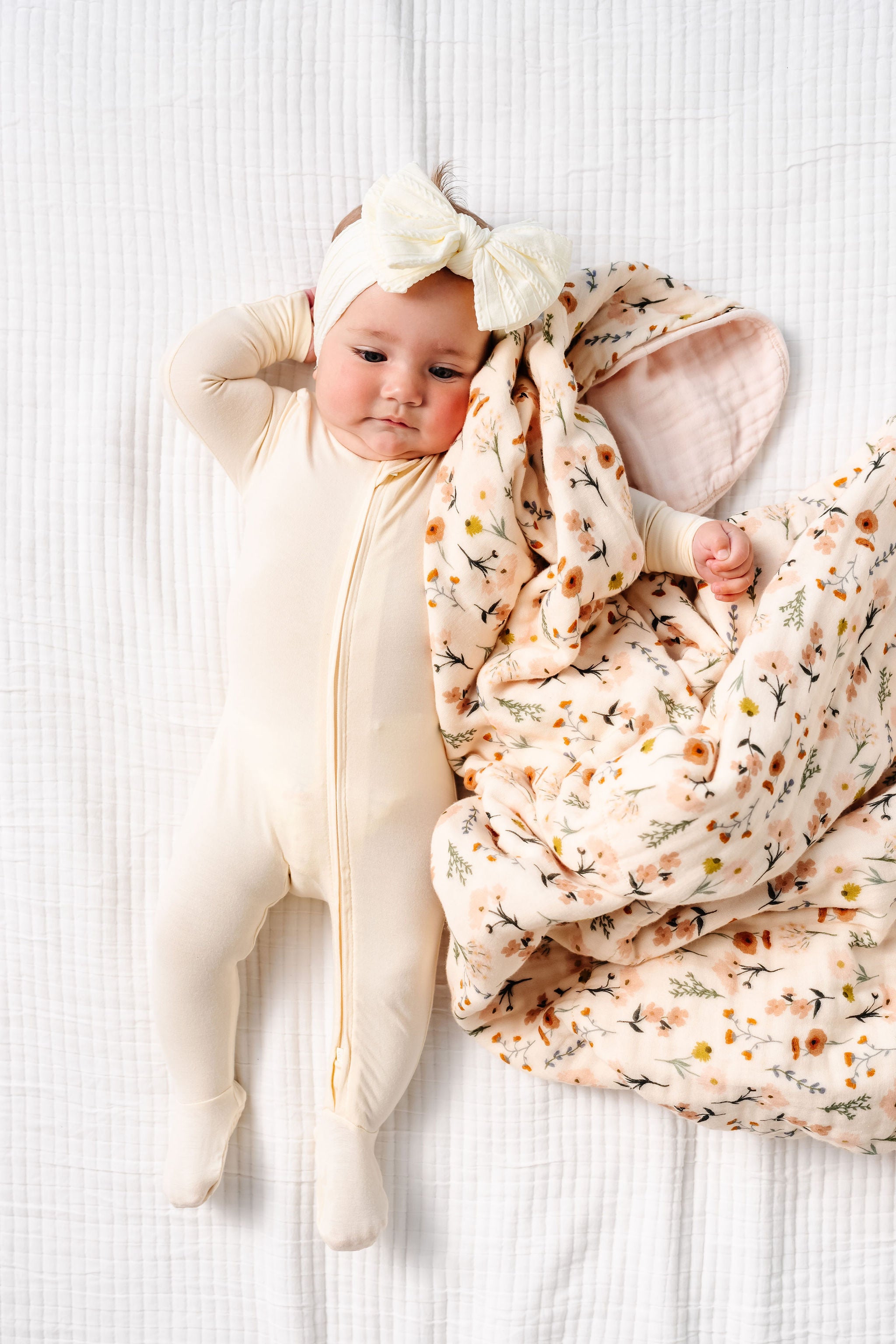 Baby wrapped in a floral blanket with a large bow on a white background