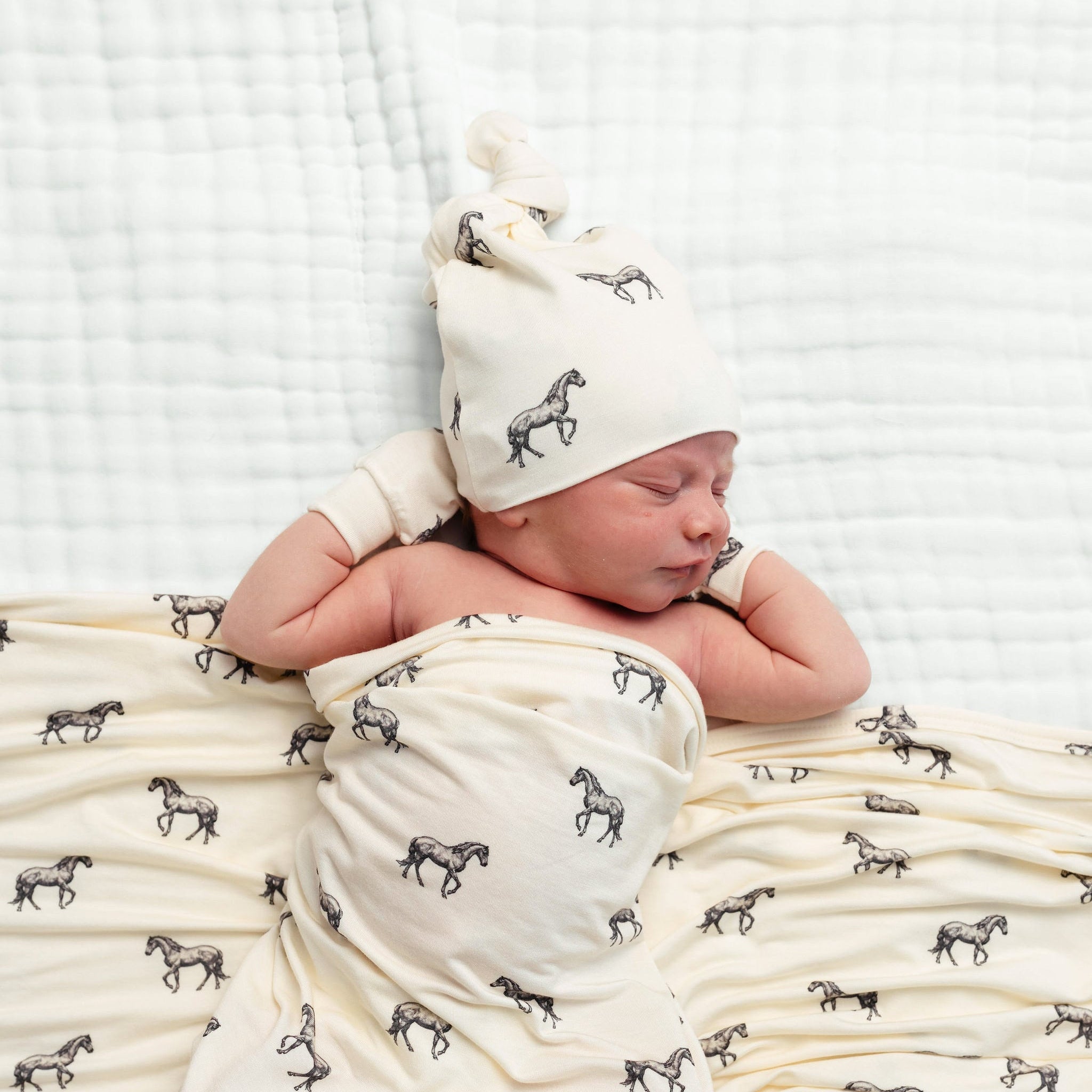 Newborn baby swaddled in a blanket with horse pattern, wearing a matching hat.