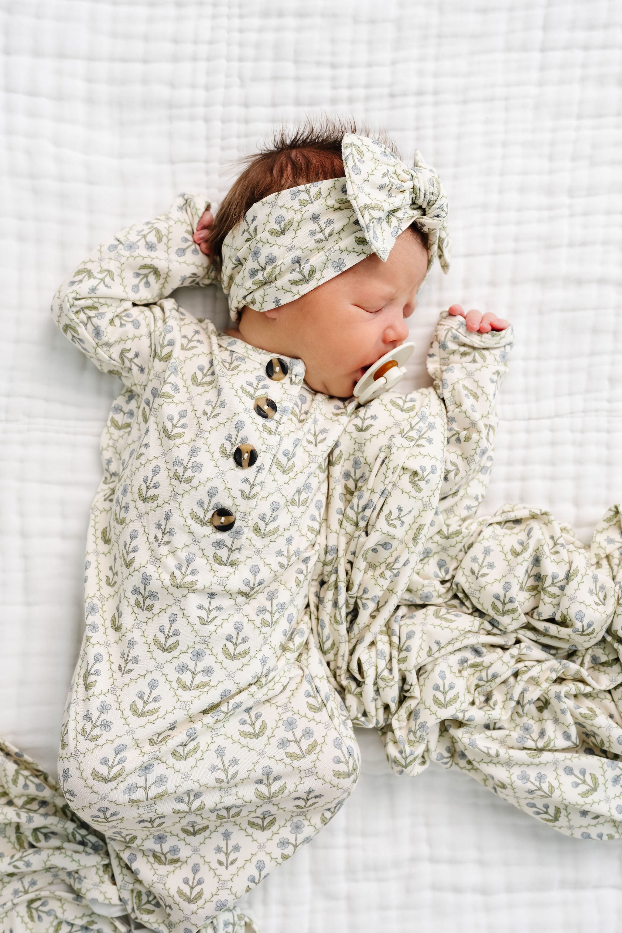 Newborn baby in floral outfit and headband on a white textured blanket
