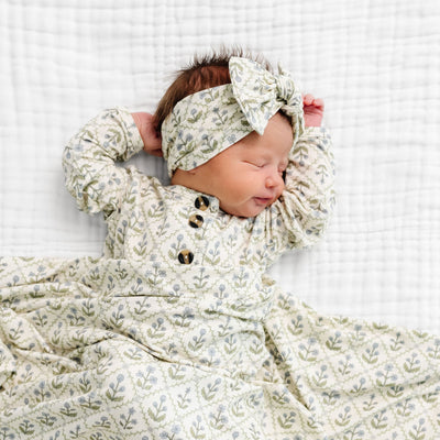 Newborn baby wrapped in a floral patterned blanket with matching headband on a white background