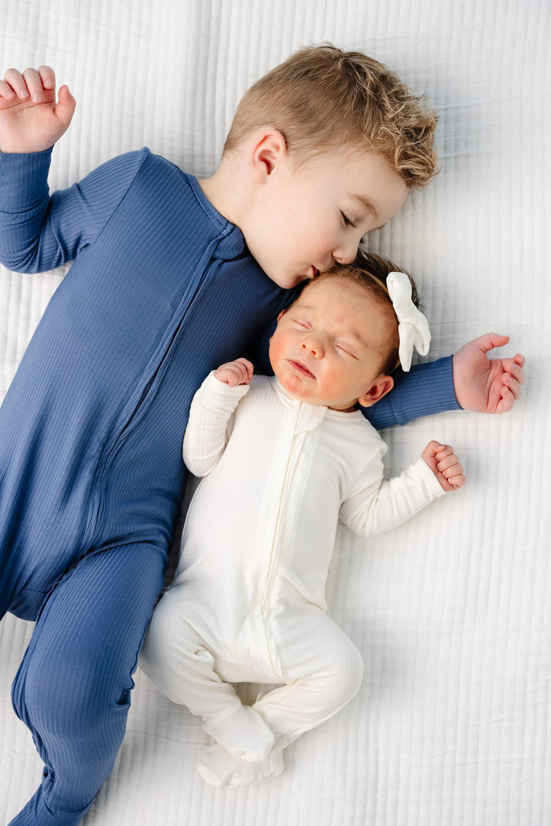 Harrison Zipper Footies Toddler boy in 2T size kissing little newborn in wren newborn size