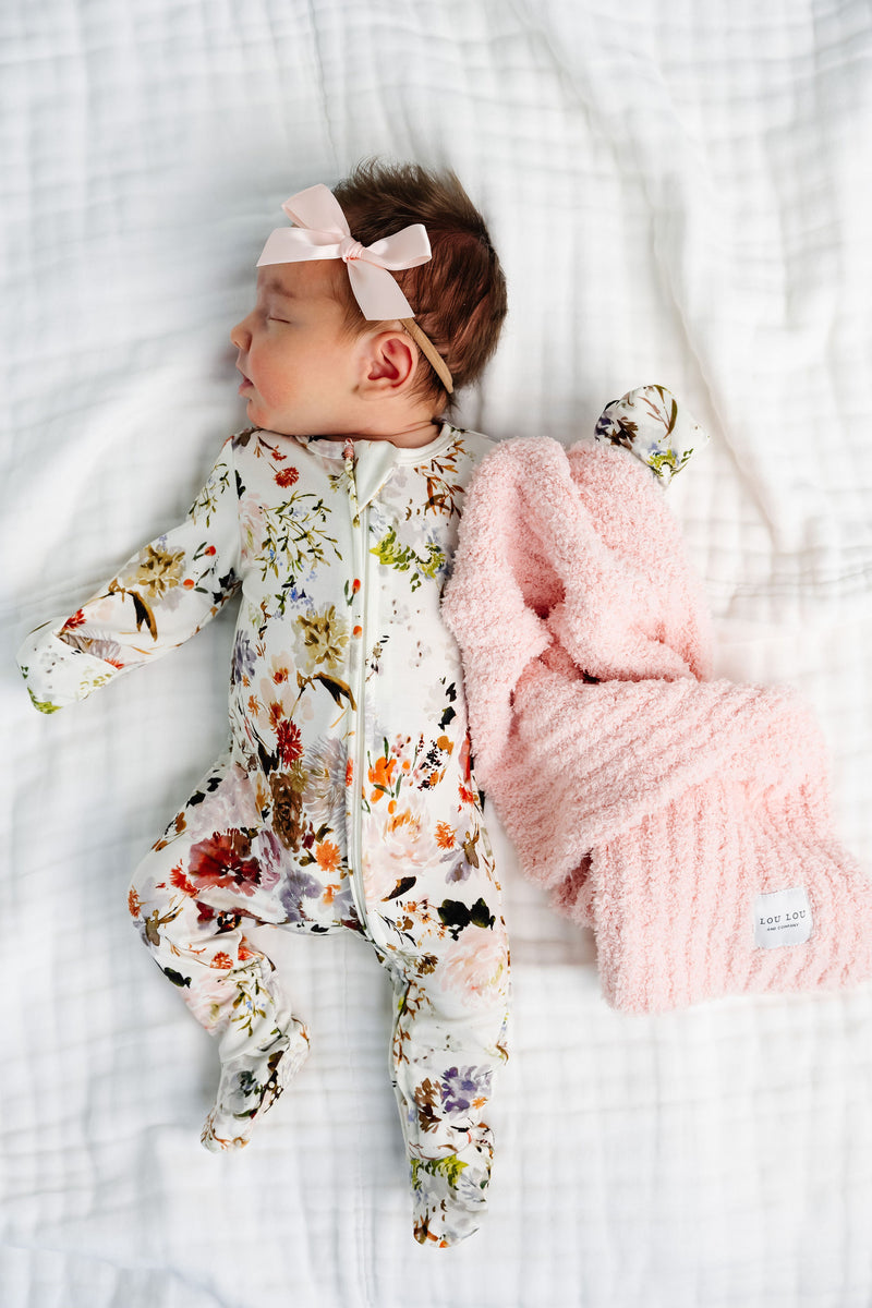 Nellie Zipper Footies baby girl in newborn size laying on bed with blush chenille mini