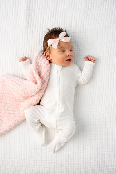 Wren Zipper Footies newborn baby girl laying on bed with blush chenille mini