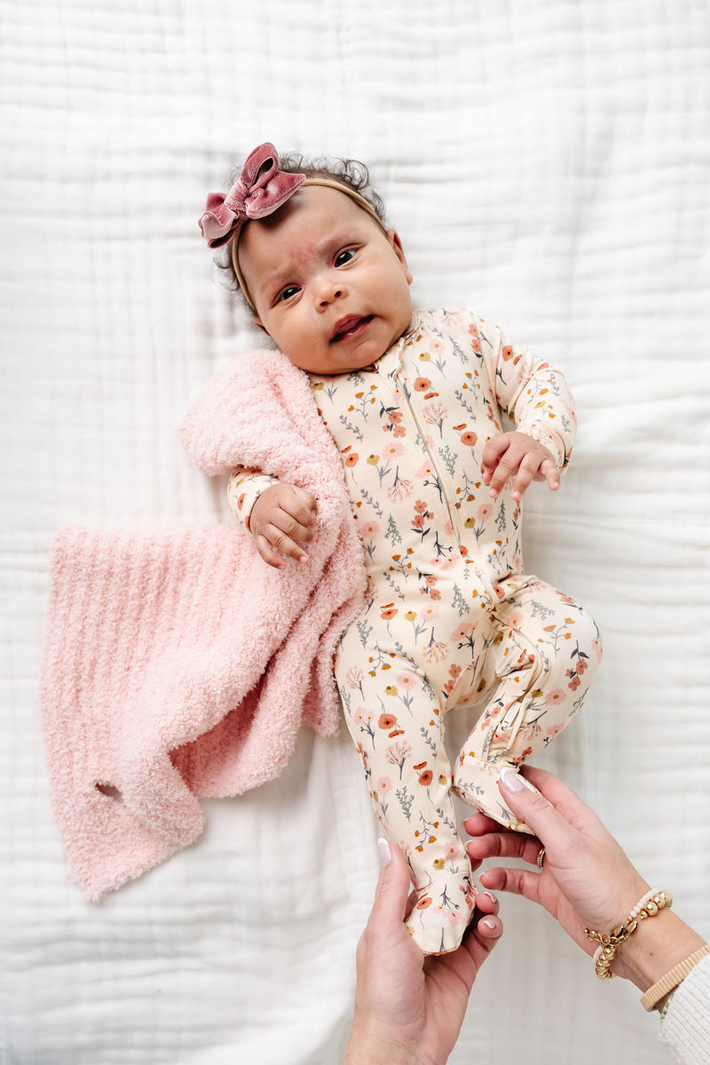 rachel zipper footies newborn girl laying on bed with blush chenille mini