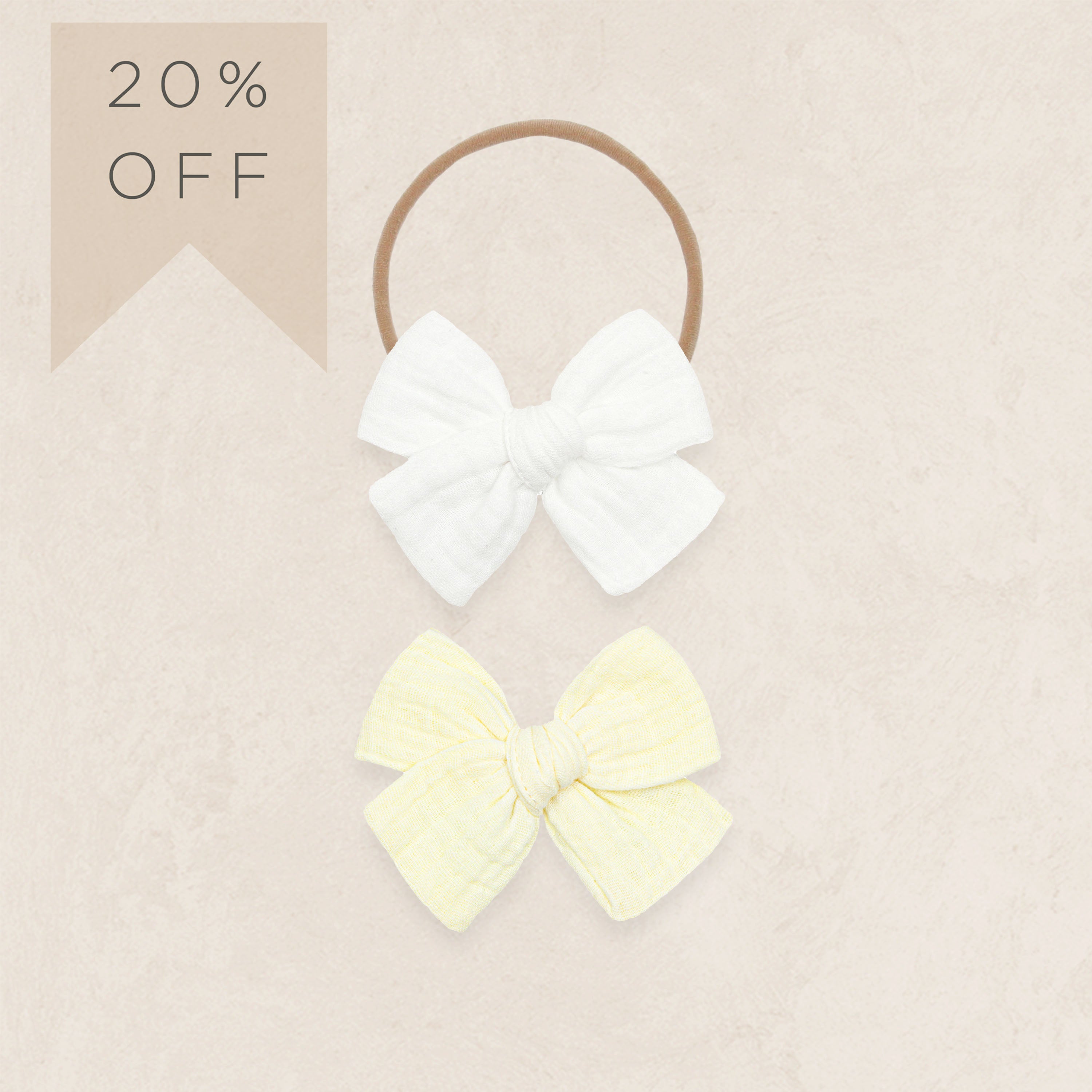Two hair bows, one white and one yellow, on a beige background with a 20% off label.