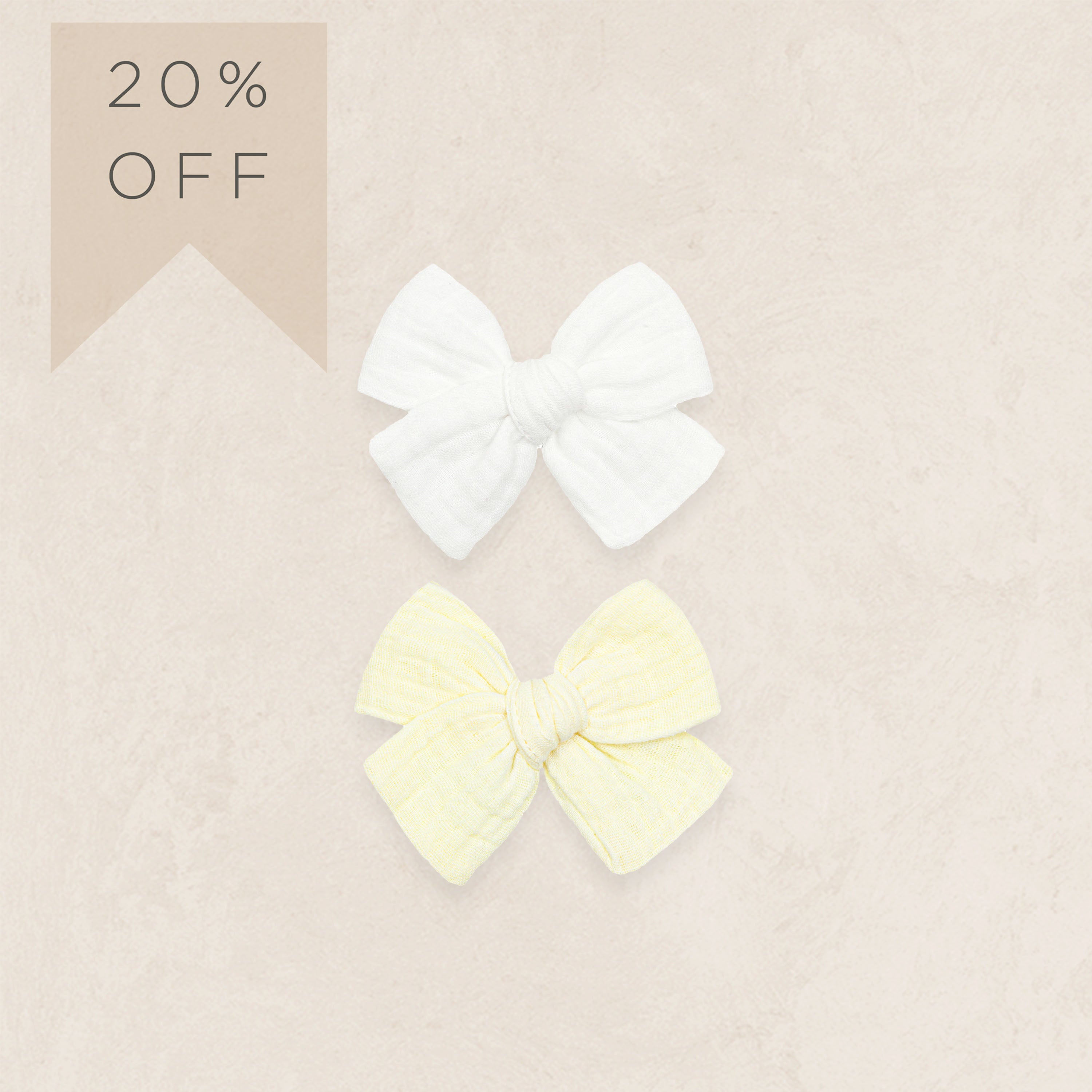 Two hair bows, one white and one yellow, on a beige background with a 20% off label.